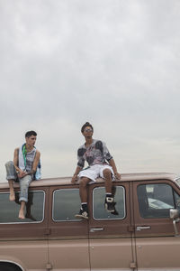 Rear view of friends sitting on car against sky