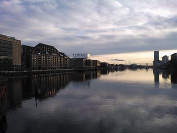 River in city against cloudy sky at sunset