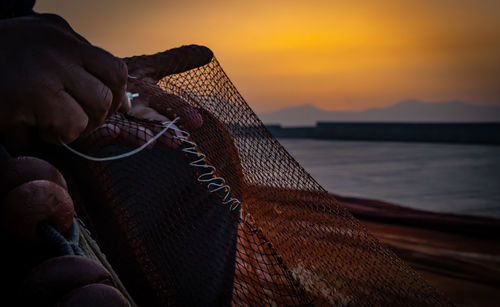 Cropped image of fisherman stitching fishnet at beach during sunset