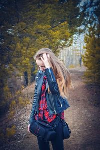 Young woman standing in forest with hand in hair during autumn