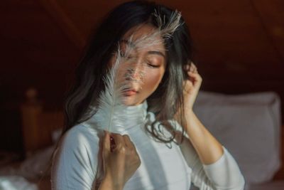 Mid adult woman with eyes closed holding feather while sitting indoors