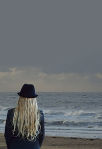 Rear view of woman standing at beach against sky