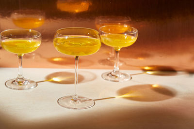 Three cocktail glassed with copper orange drinks on neutral table with long shadows and copy space