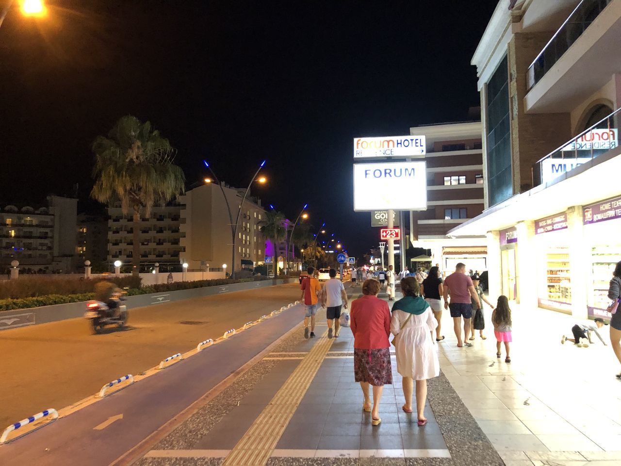 GROUP OF PEOPLE WALKING ON ROAD ALONG BUILDINGS AT NIGHT