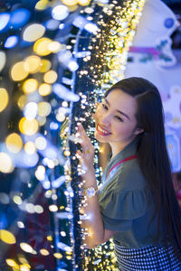 Portrait of smiling woman standing by illuminated lights at night