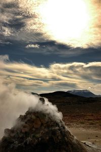 Smoke emitting volcanic landscape against sky