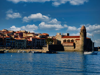 View of buildings by river against cloudy sky