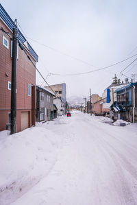 Snow covered houses by buildings in city against sky