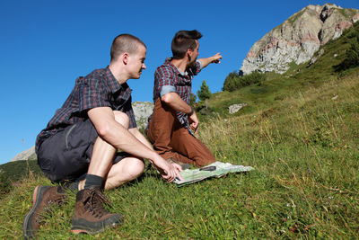 Friends sitting on grass against mountain