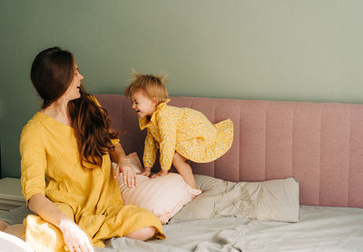 A little toddler daughter jumps on the bed and plays with a caring mother.