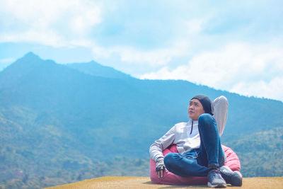 Portrait of man sitting on mountain against sky