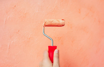 Repair roller in the left hand of a person paints wooden plywood in pastel soft orange color