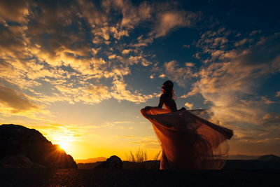 Silhouette woman standing on land against sky during sunset