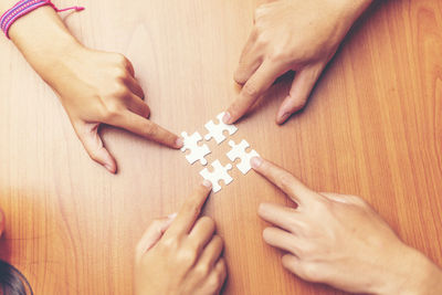 Cropped hands of friends playing jigsaw puzzle on wooden table