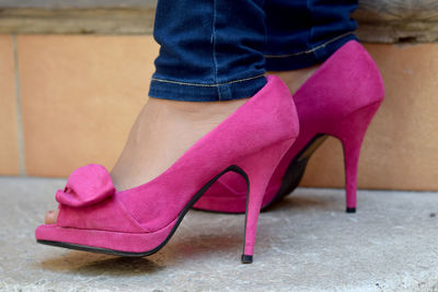 Low section of woman wearing pink high heels standing on footpath
