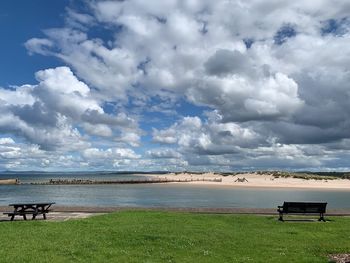 Empty bench on shore by sea against sky