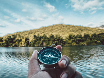 Midsection of person holding umbrella by lake against sky