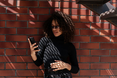 Pretty woman with curly hair using smartphone in the city