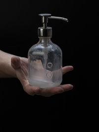 Close-up of hand holding bottle against black background