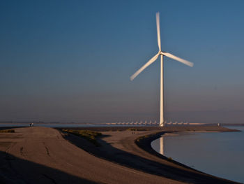 Windmill on beach against sky during sunset