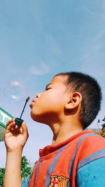 Low angle view of boy blowing bubble against sky