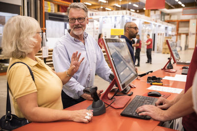 Senior male and female customers talking with each other while standing at checkout counter in hardware store