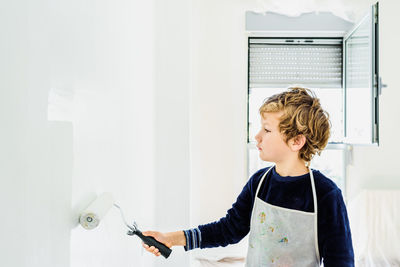 Cute boy painting wall at home