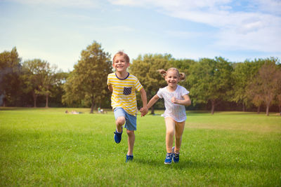 Full length of smiling sibling running on grass at park