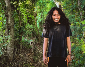 Portrait of smiling young man standing against trees in forest