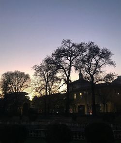 Silhouette tree by building against sky at dusk