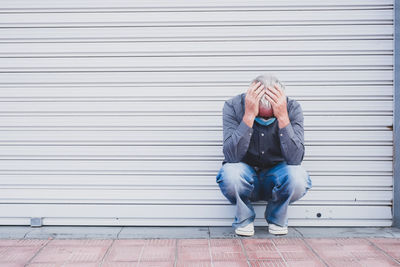 Full length of senior man in mask crouching by closed shutter