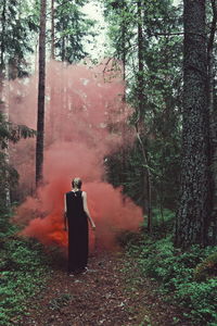 Rear view of woman walking by red smoke in forest