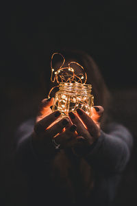 Woman holding illuminated string lights in jar at night