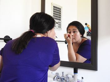 Reflection of woman in mirror while applying eyeliner at home