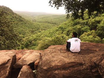 Rear view of man sitting on rock