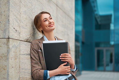 Portrait of a smiling young woman standing against wall