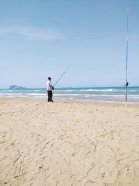 Man fishing at beach against sky