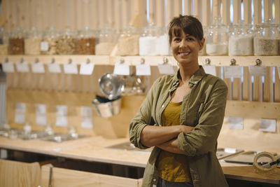 Smiling businesswoman with arms crossed standing against glass jar in cafe