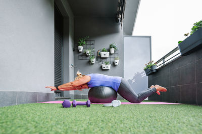 Full length profile of elderly woman in sportswear balancing on fit ball at balcony