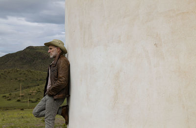 Adult man in cowboy hat standing against white wall in field