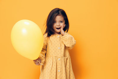 Portrait of young woman with balloons against yellow background