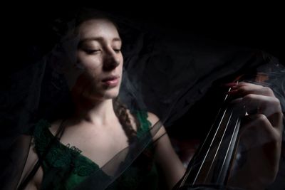Close-up of young woman playing string instrument in darkroom