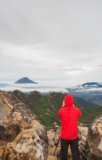 Rear view of woman standing on rock by sea against sky