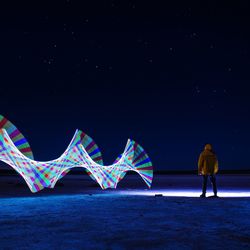 Rear view of man standing by light painting against sky at night