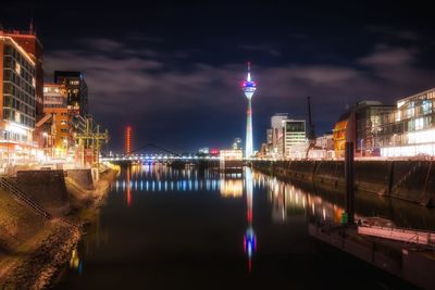 Illuminated buildings by river against sky at night