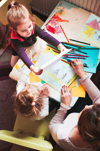 High angle view of mother and daughters painting on paper at home