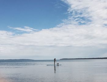 Woman with dog standing on paddleboard over sea against sky