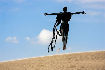 Young man in costume jumping at desert against sky