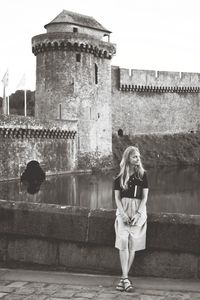 Woman standing against wall and building against sky