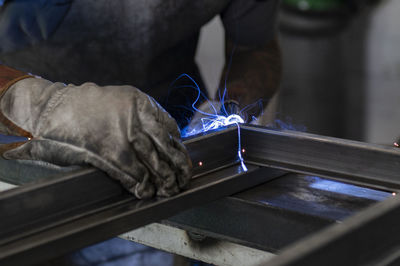 Unrecognizable male welder using welding machine on metal detail while working at workbench in factory